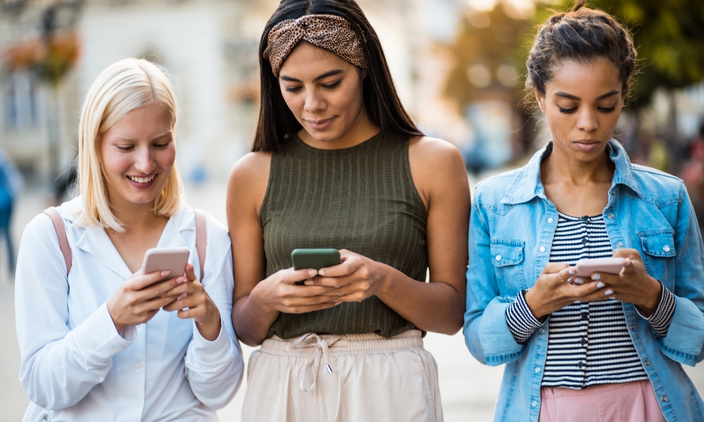 three women standing outside looking at iphones