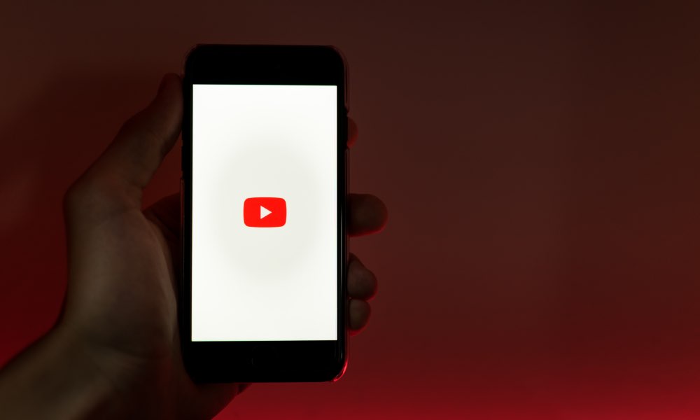 Person holding iPhone with YouTube app running.