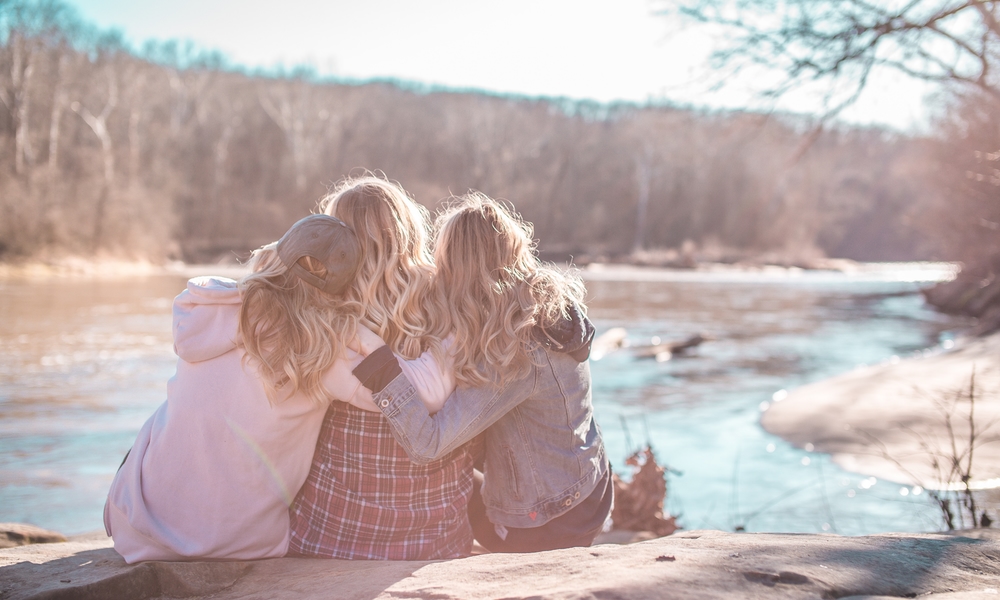 three women sitting on edge of lake enjoying life