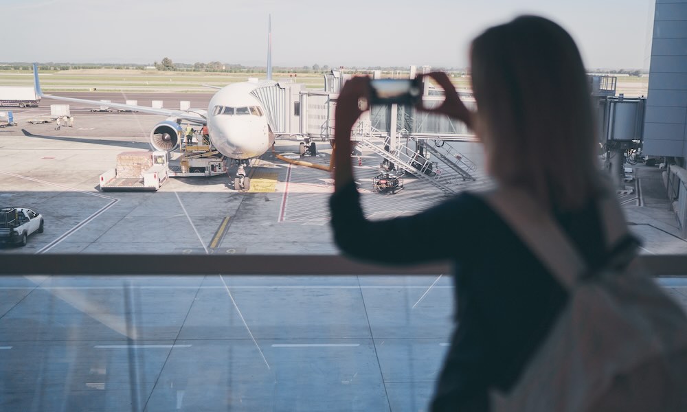 Travel concept. Woman taking photo of plane while waiting for boarding in airport terminal.