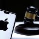 Stafford, United Kingdom December 15 2020: Apple logo seen on the smartphone placed next to the judges gavel. Concept for a lawsuit, legal case, antitrust and fine. Real photo, not a montage.
