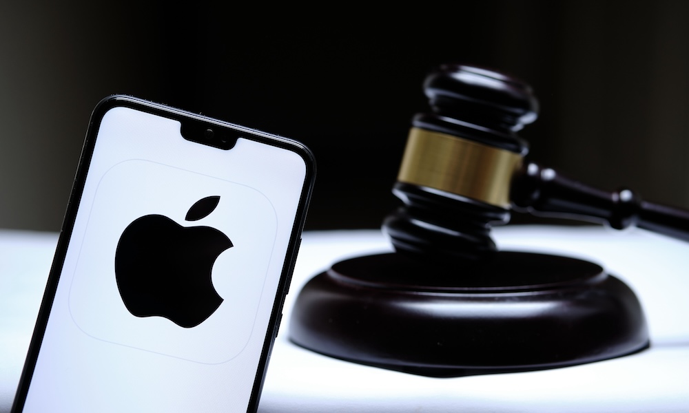Stafford, United Kingdom December 15 2020: Apple logo seen on the smartphone placed next to the judges gavel. Concept for a lawsuit, legal case, antitrust and fine. Real photo, not a montage.