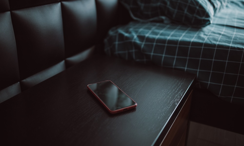 Smartphone on nightstand near bed in hotel room. Modern interior