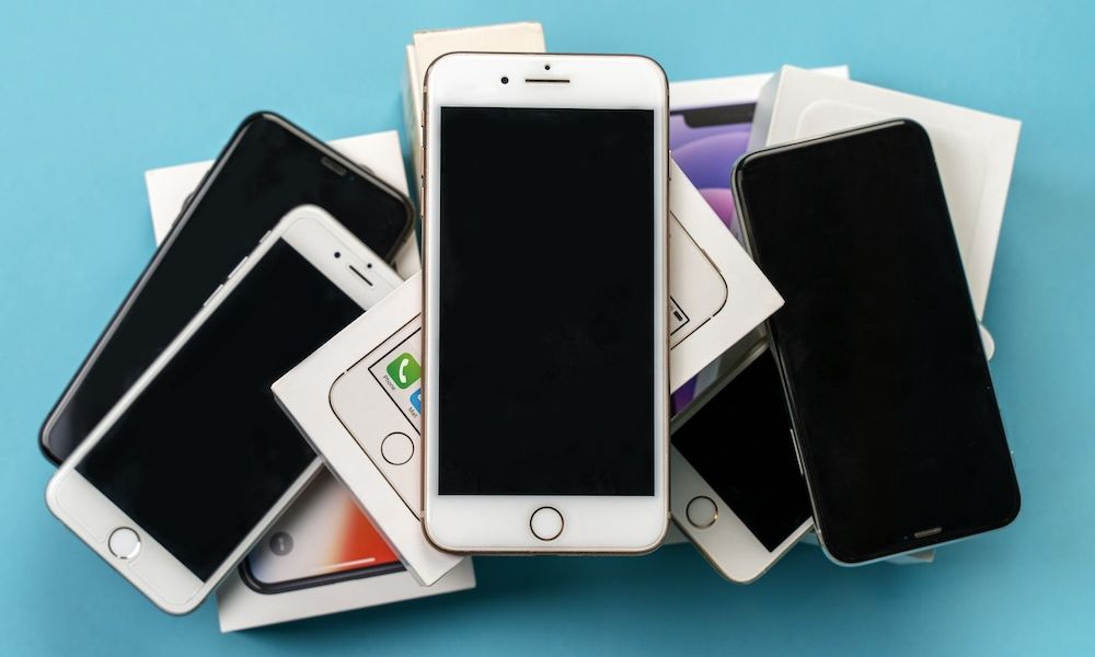 ROSTOV ON DON, ROSTOV REGION / RUSSIA Dec.16 2021: Pile of used mobile phones Apple iPhone, black and white, lying down with their boxes on blue background. Copy space.