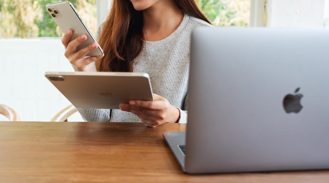 Jun 16th 2020 : An asian woman holding and using Iphone 11 Pro Max smart phone and Apple New Ipad Pro 2020 tablet pc with Apple MacBook Pro laptop computer on wooden table , Chiang mai Thailand