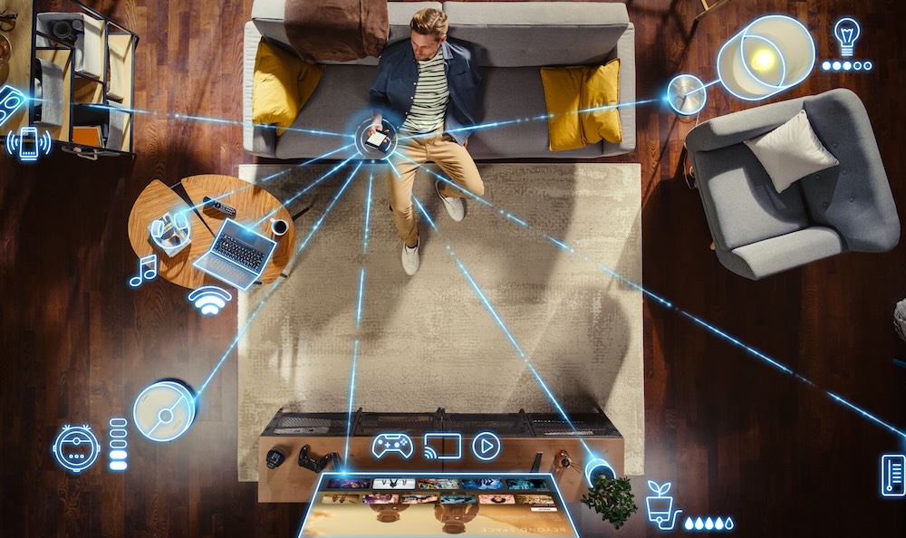 Top View Of Caucasian Man In the Loft Apartment Sitting Down on The Couch and Connecting Smartphone to Convenient Smart Home System. VFX Edit Visualizing Connected Devices. Laptop, TV, Speaker.