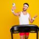 Photo of cool cheerful guy sportswear running treadmill recording vlog device empty space isolated yellow color background