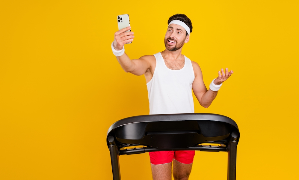 Photo of cool cheerful guy sportswear running treadmill recording vlog device empty space isolated yellow color background