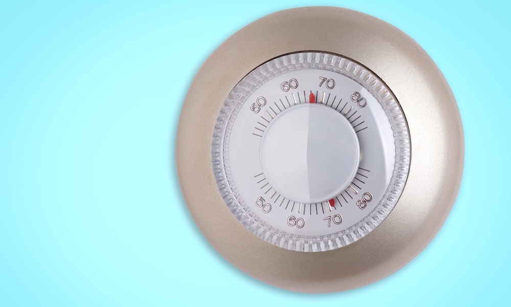 Round thermostat dial on a blue background adjusting temperature settings
