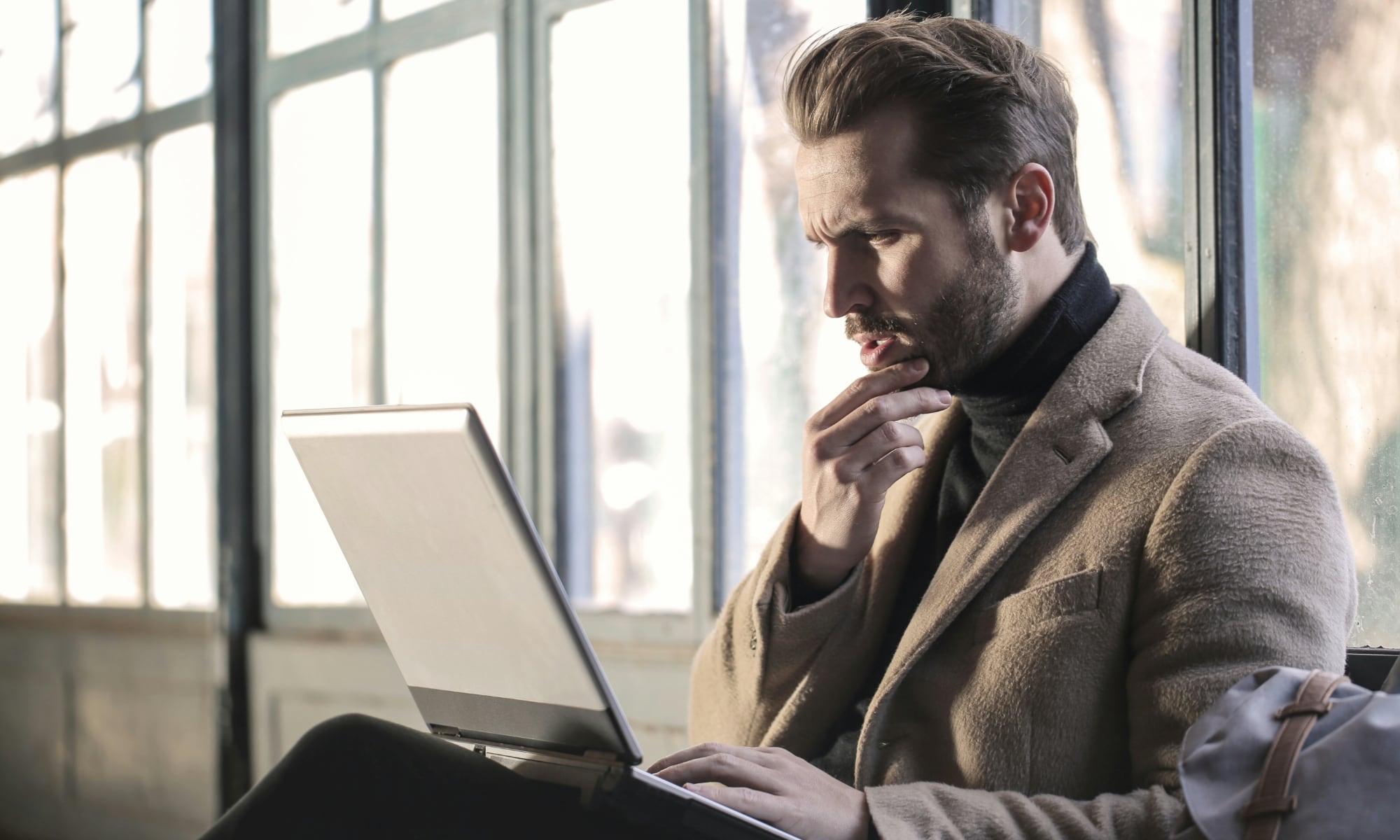 man looking at laptop scratching his chin in confusion