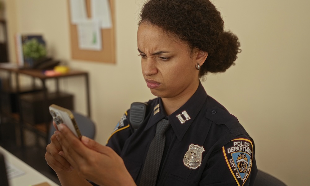 Young woman police officer intently examines smartphone in office setting showcasing dedication and focus in law enforcement environment.