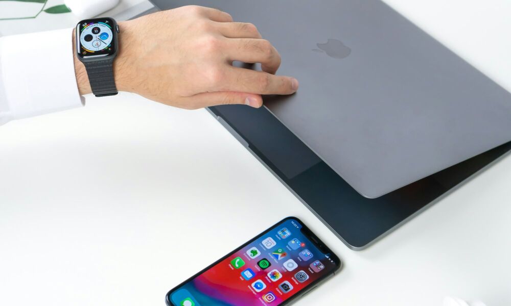 person opening MacBook wearing Apple Watch with iPhone person opening MacBook wearing Apple Watch with iPhone