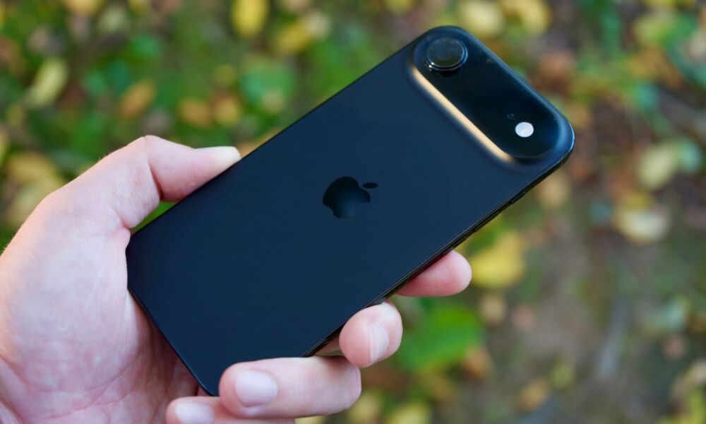 person holding iPhone Air against green outdoor background