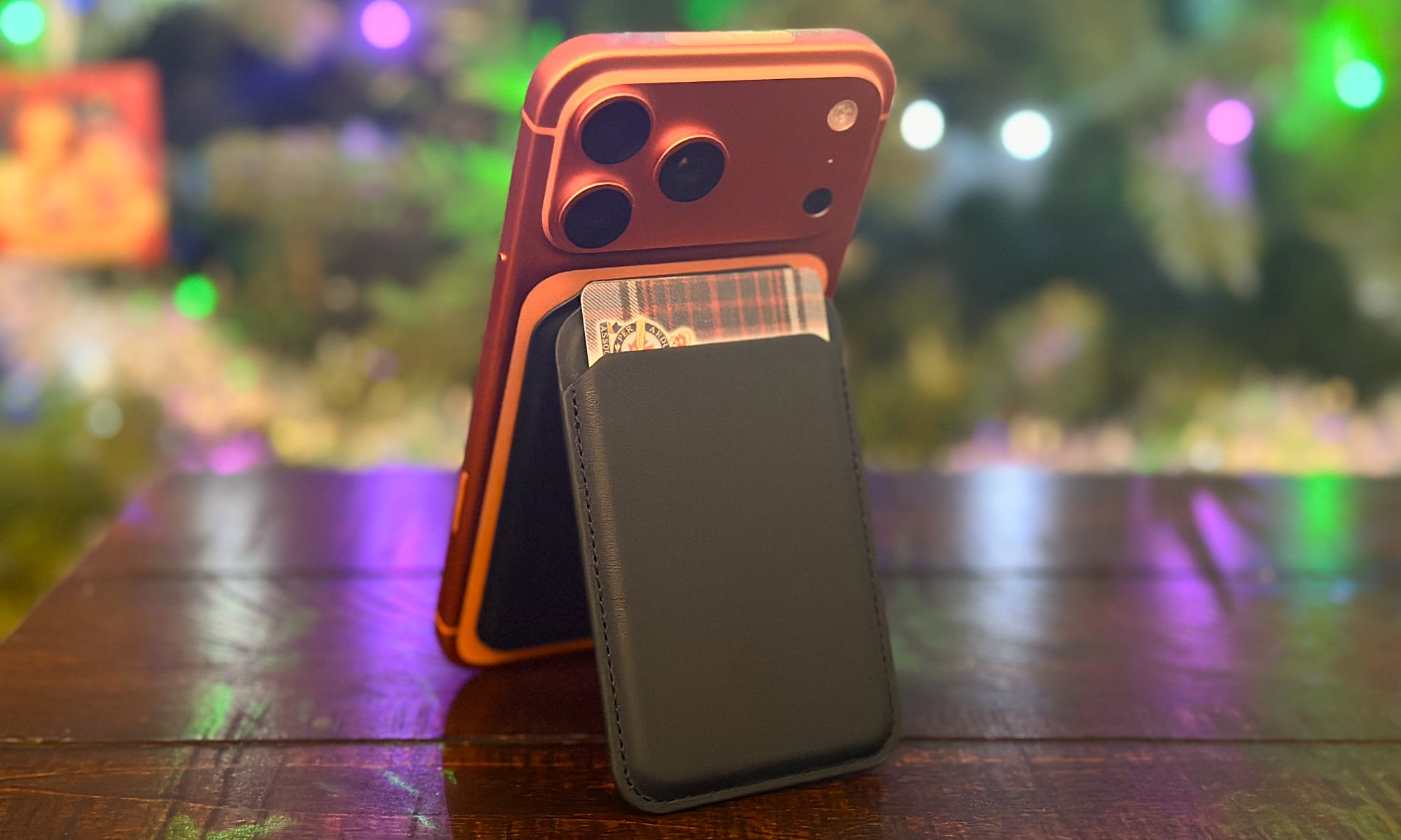 Orange iPhone 17 Pro Max propped up using Satechi's blue Magnetic Wallet Case with a Christmas tree in the background.