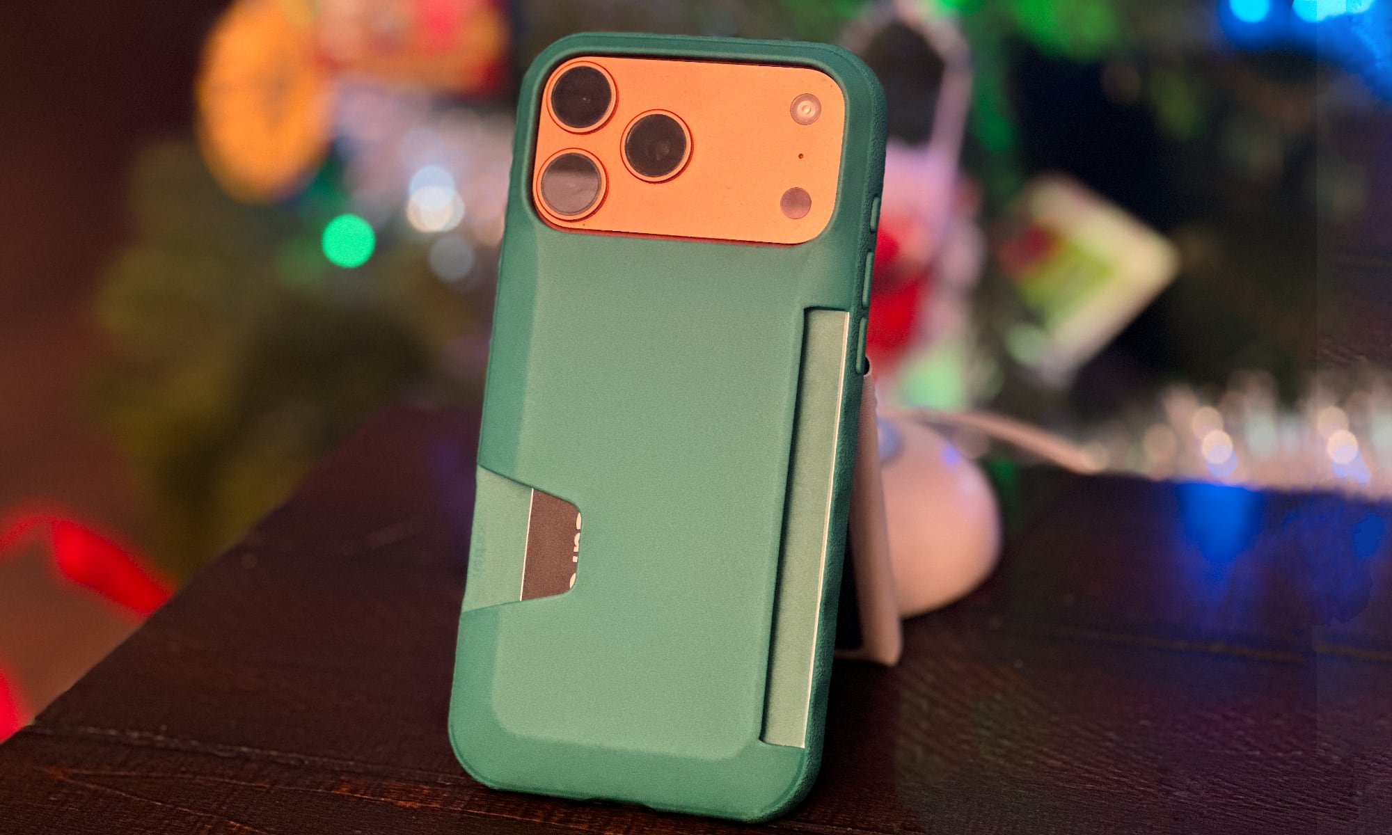 Smartish Wallet Slayer case for iPhone 17 Pro Max in "So Jaded" green color standing on a table with a Christmas tree in the background.