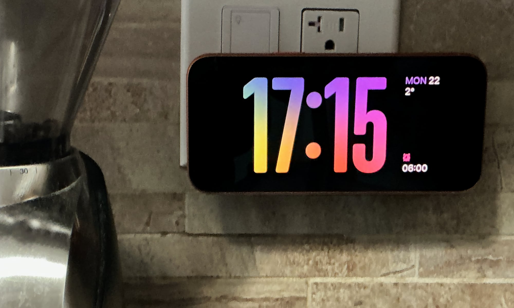 iPhone 17 Pro Max showing clock in StandBy mode on a TwelveSouth PowerBug Charger plugged into a kitchen wall outlet.
