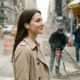 A woman wearing AirPods Pro walks calmly and smiles while navigating a chaotic city street. In the background, yellow taxis drive past and construction workers use a jackhammer, contrasting the noisy environment with her peaceful demeanor.