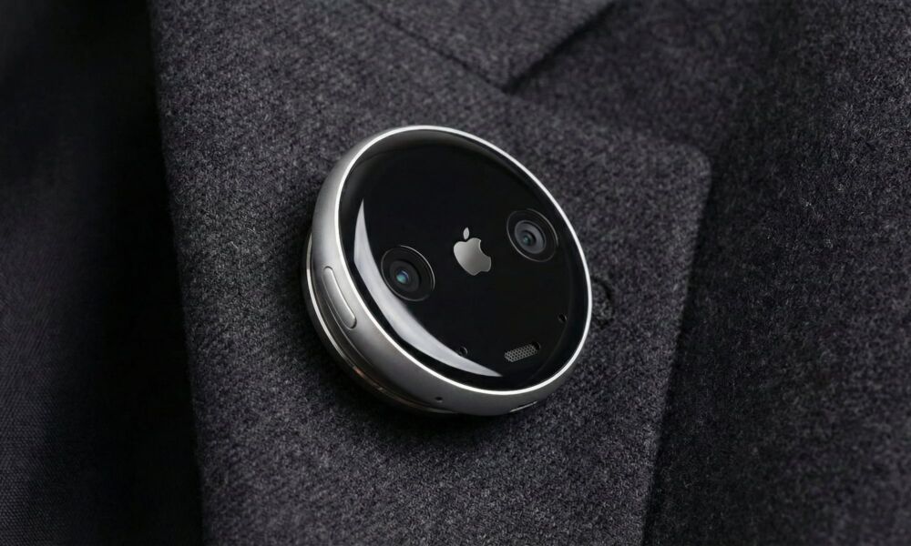 A concept design of a circular Apple AI pin attached to a charcoal grey suit lapel. The device features a polished aluminum rim, a black glass face with a small silver Apple logo in the center, and two visible camera lenses on either side. A physical button is visible on the side of the thin, disc-shaped wearable.