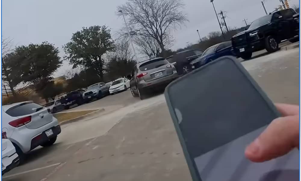 A screenshot from an Instagram reel by user iflipiphones showing a person chasing a silver sedan through a parking lot. The person in the foreground is holding an iPhone toward the escaping vehicle, which is driving away after a theft during a sales meetup in Keller, Texas.