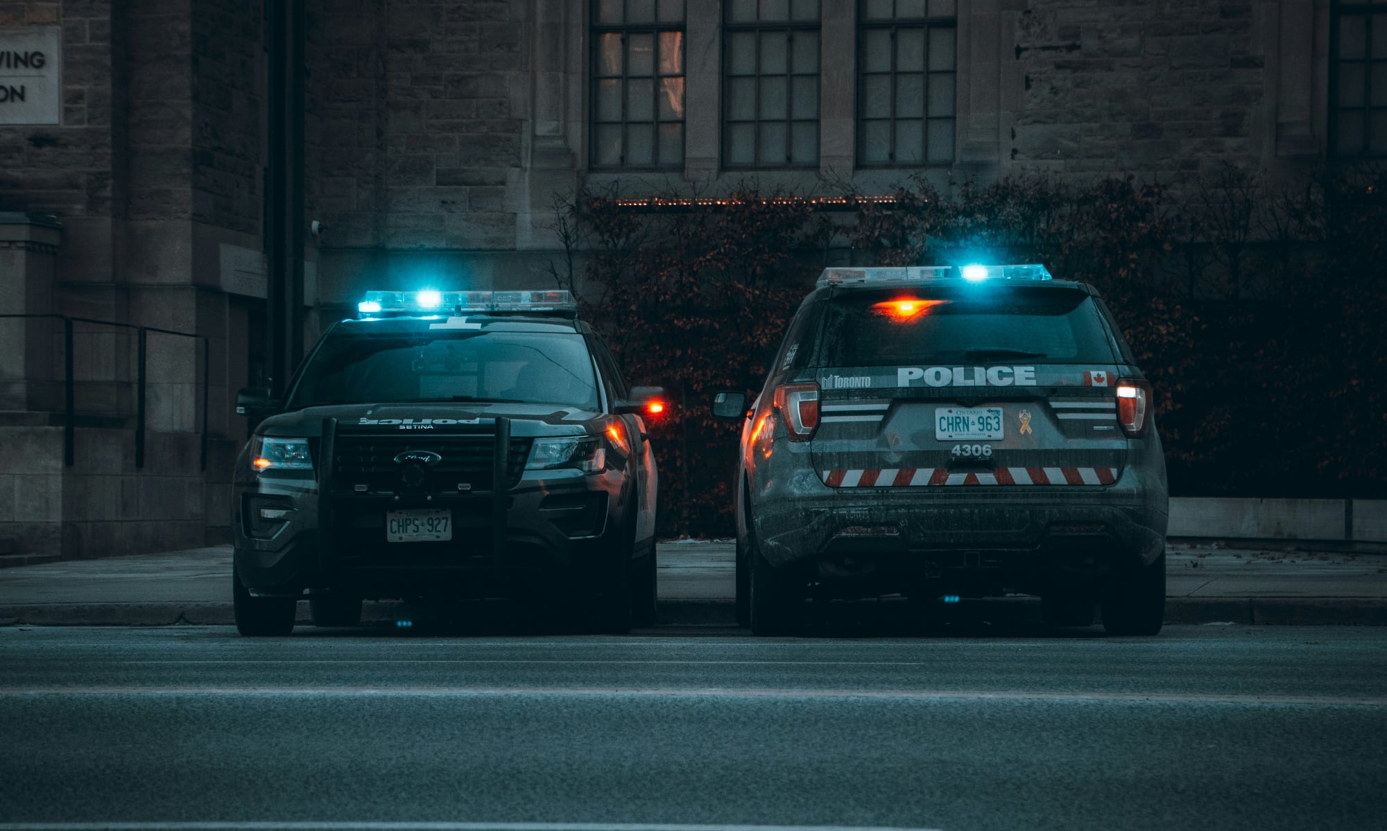 Two Toronto Police Service cruisers parked on a city street with the distinct white and grey livery.