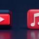 A side-by-side 3D render of the YouTube play button icon and the Apple Music note icon against a unified dark background, illustrating how the services complement each other.