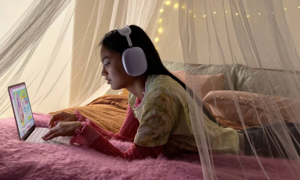 Girl laying on bed using a MacBook Neo while wearing AirPods Max.