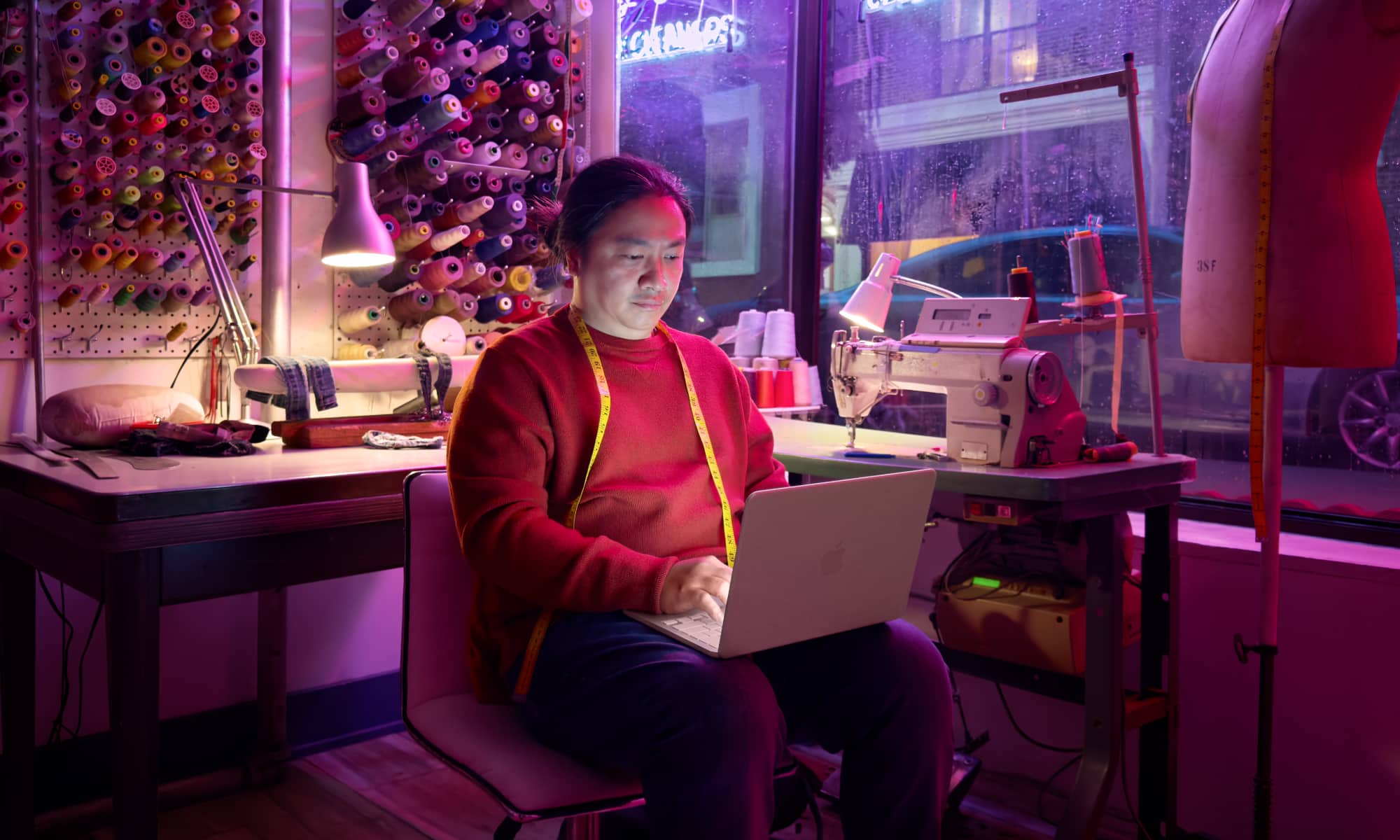 A creative professional using a blush-colored MacBook Neo in a modern tailor shop environment.