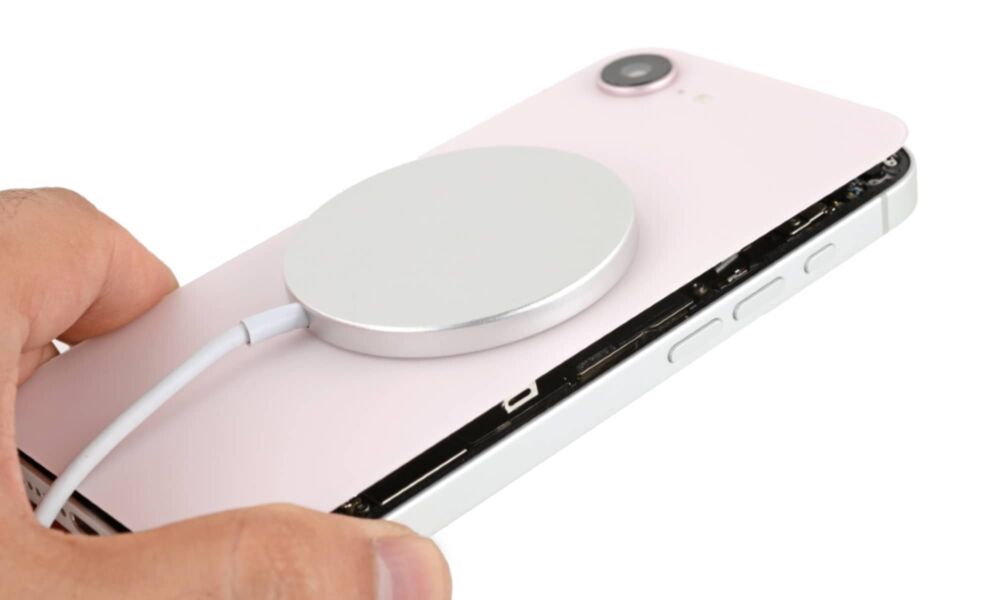 Person holding an iPhone 16e with a soft pink iPhone 17e glass back with a MagSafe charger attached to it.