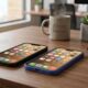 A landscape photograph showing the black iPhone 17e with a classic notch and the ultramarine blue iPhone 16 with a Dynamic Island resting side-by-side on a polished walnut office desk, next to a ceramic latte mug and a green succulent plant.