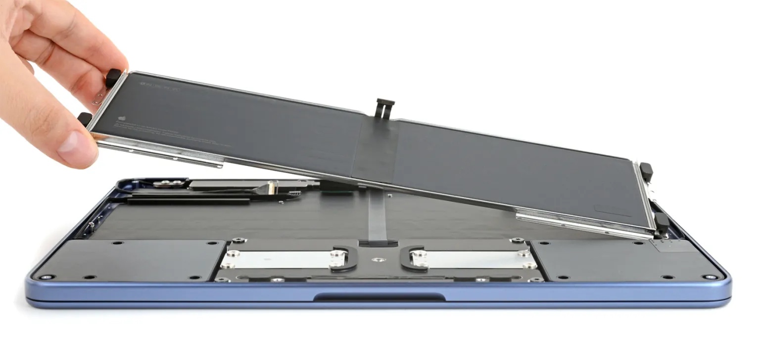 A technician removing one of the 18 screws securing the MacBook Neo battery to its internal tray during an iFixit teardown.