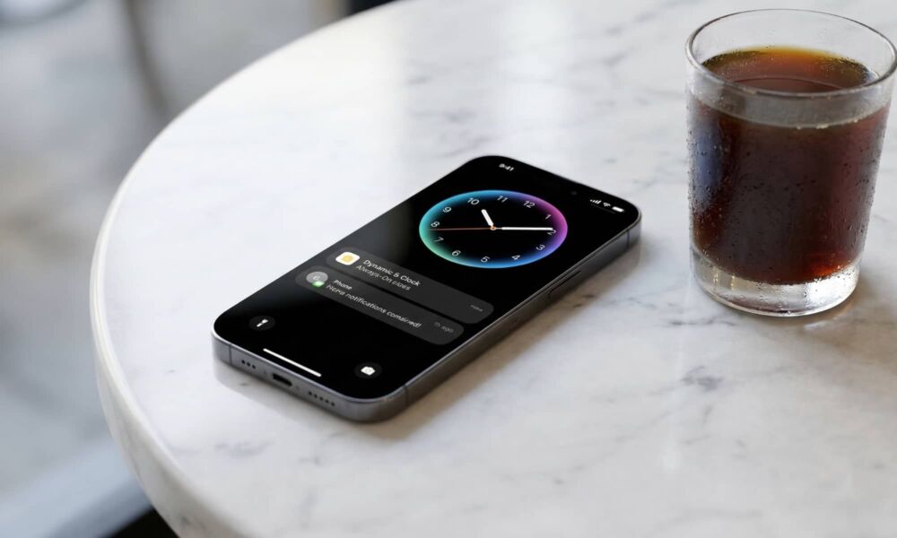 A sleek iPhone 19e concept sitting on a minimalist marble cafe table next to a glass of cold brew, its screen showing a vibrant always-on clock with smooth fluid animations.