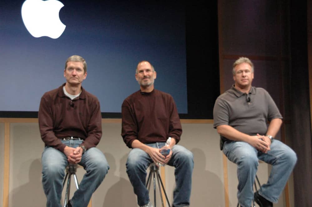 Tim Cook, Steve Jobs, and Phil Schiller sitting on stage at the iMac launch event on August 7, 2007.