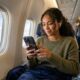 Woman using iPhone offline on airplane for pre-downloaded entertainment.