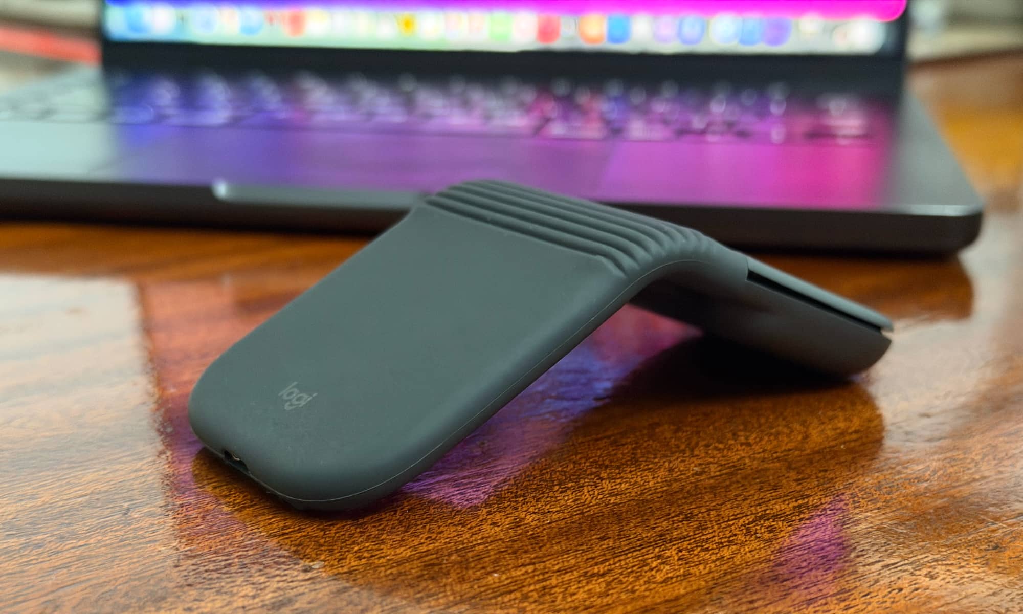 A Logitech Mobi Fold on a wooden table in front of a MacBook Pro.