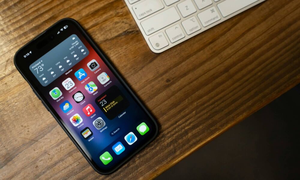 An iPhone sitting next to a Magic Keyboard on a wooden table.