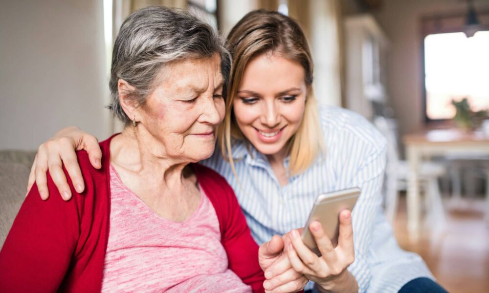 An elderly grandmother and her granddaughter using a smartphone at home.