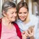 An elderly grandmother and her granddaughter using a smartphone at home.