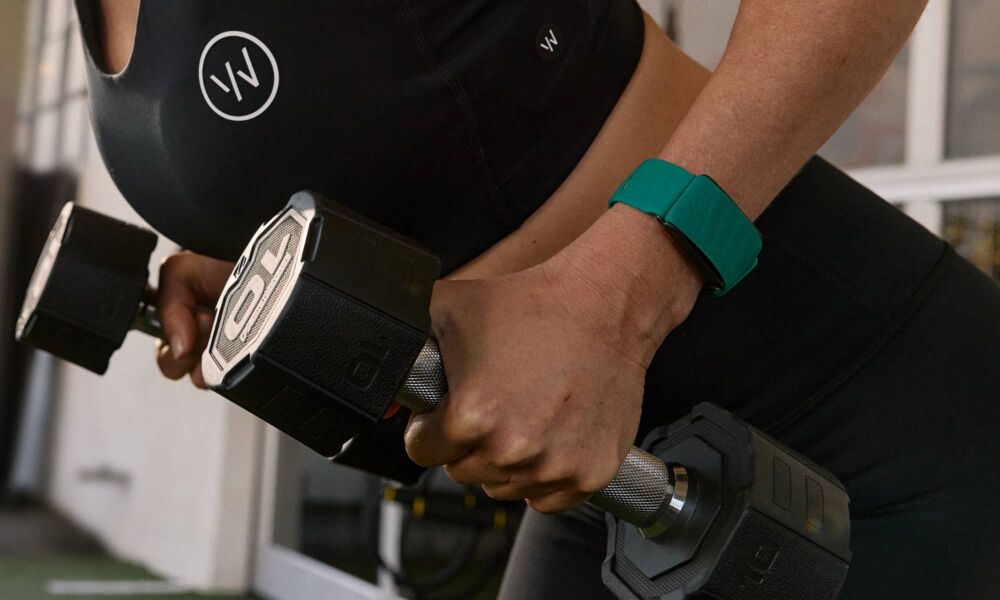 Woman wearing green Whoop fitness band while lifting weights.