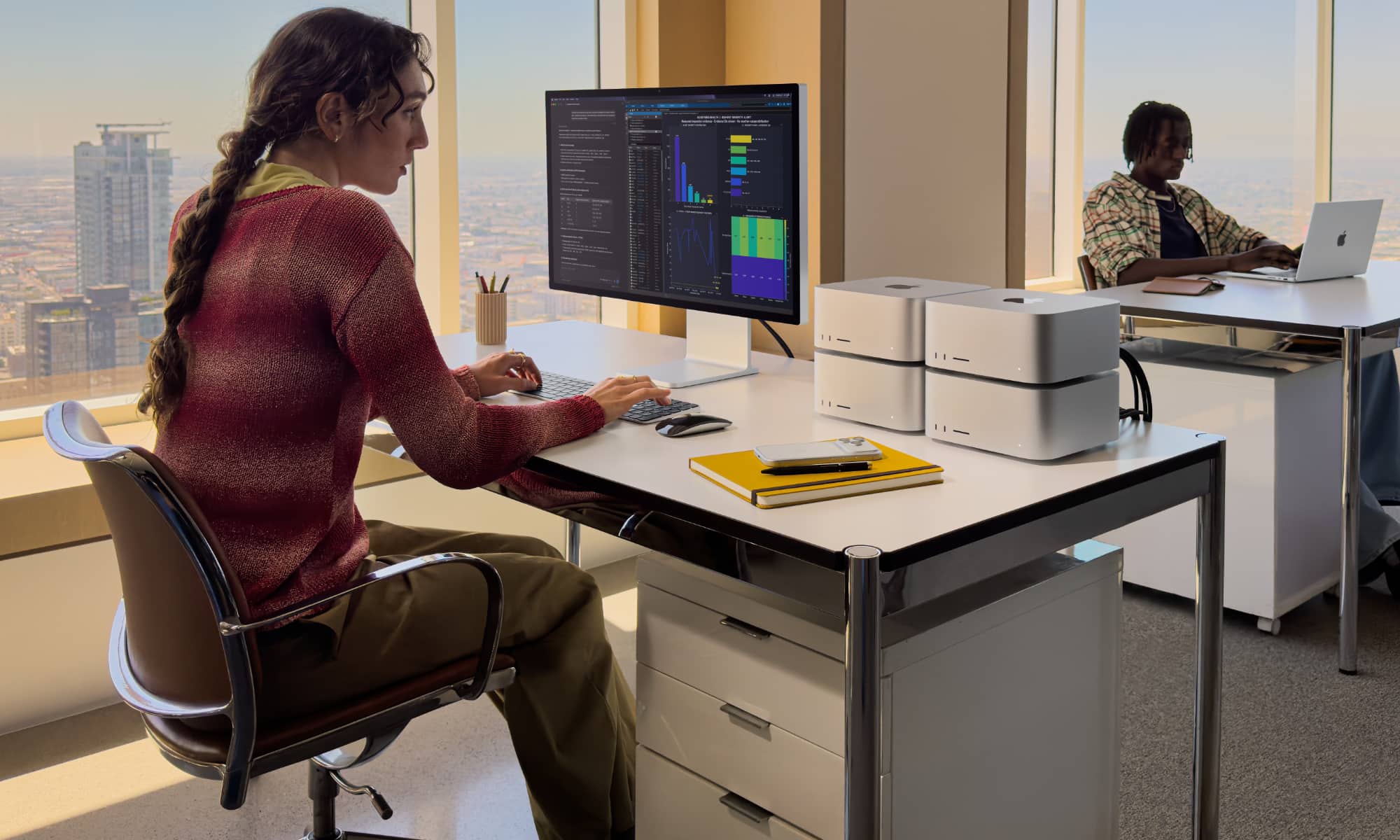 Woman in a modern high-rise office working at a desk with four Mac Studio computers an an Apple Studio Display.