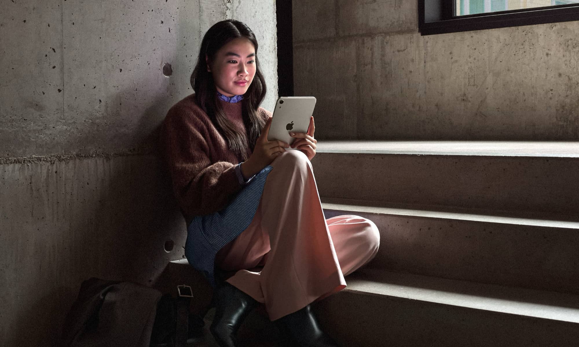 Young woman sitting on concrete steps looking at an iPad mini.