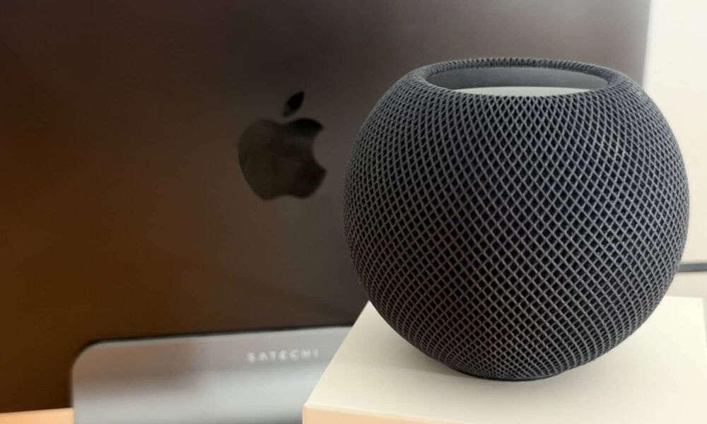HomePod mini 2 speaker with docked MacBook Pro in background.