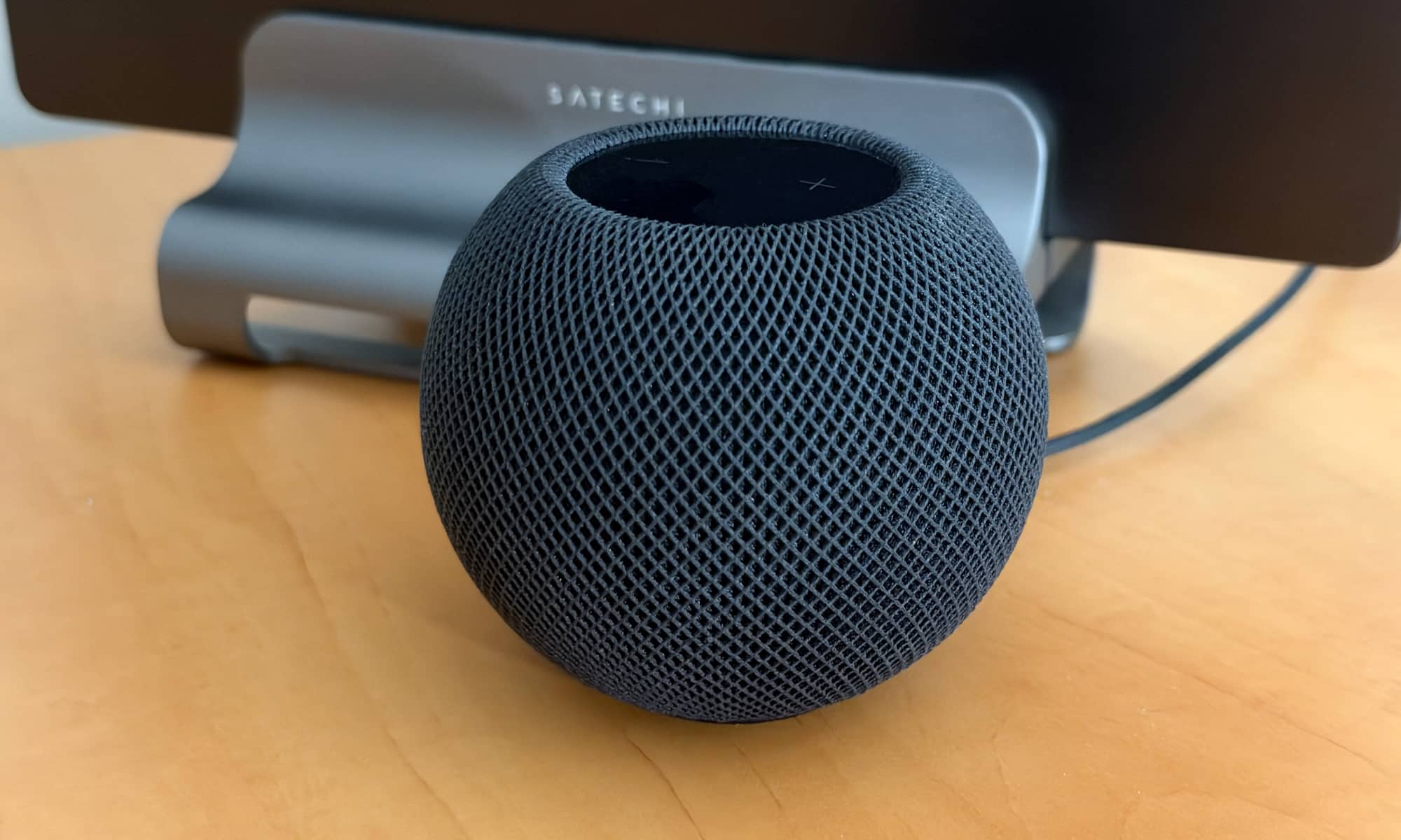 HomePod mini 2 speaker with docked MacBook Pro in background.
